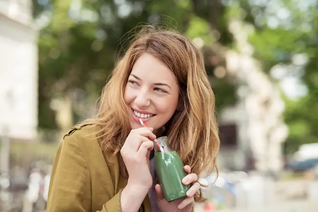 Una joven mujer bebiendo un batido verde que impulsa la serotonina en todo el cuerpo