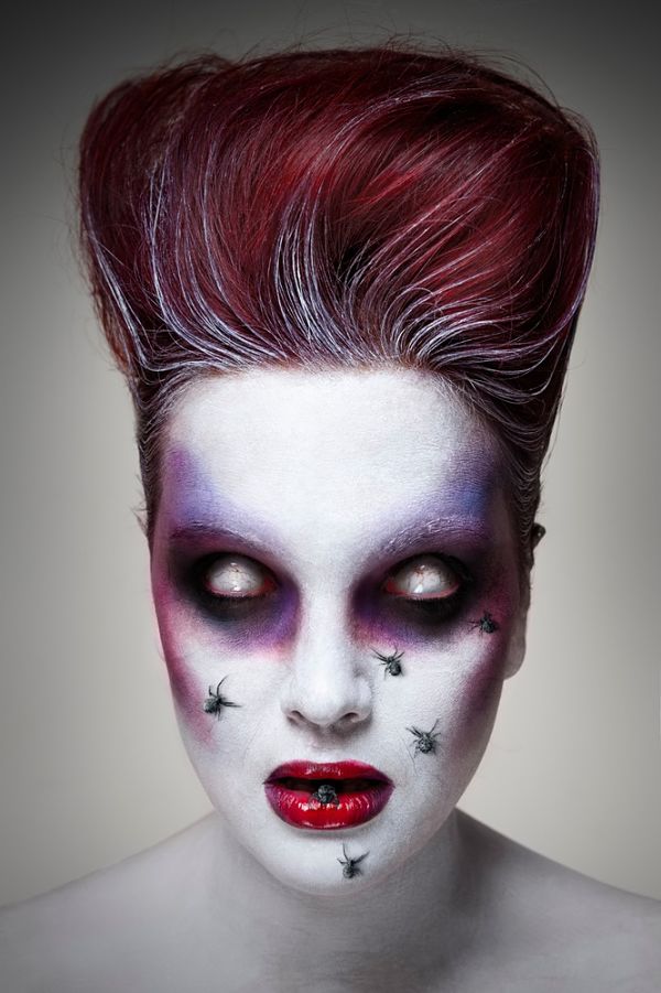 maquillaje para halloween que tiene forma de muerto viviente con ojos blanco y arañas en la cara