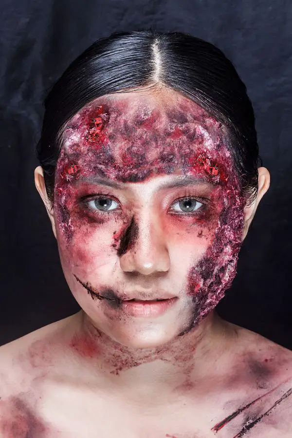 mujer con maquillaje para Halloween con el rostro pintado con heridas de color rojo