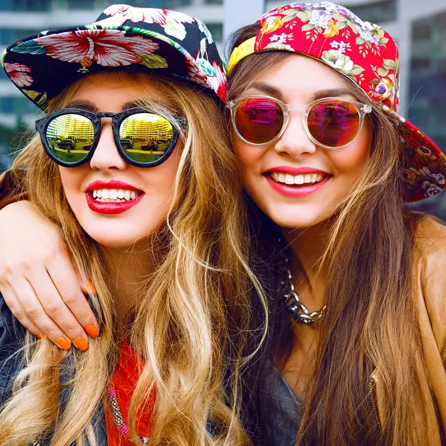 Chicas jóvenes luciendo unas monturas de gafas con vidrios de colores y redondeadas, al mejor estilo retro