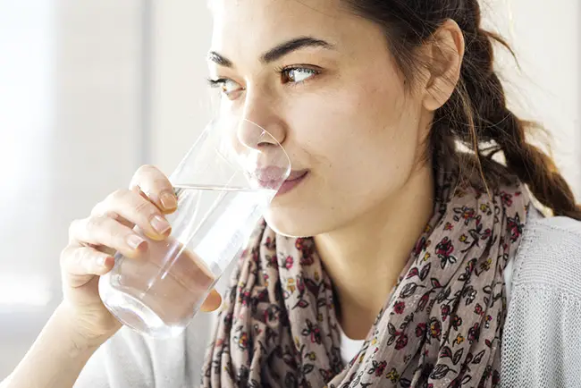 Mujer tomando un vaso de agua para aliviar el hipo persistente