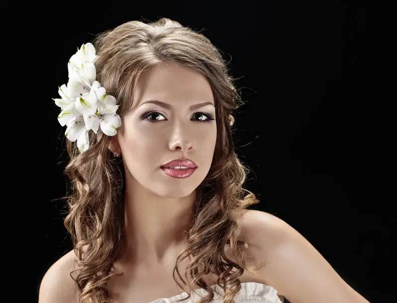Joven mujer dejando su cabello suelo con una flor al costado, un clásico look de novia en primavera