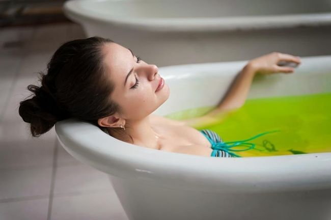 Mujer se baña en una tina con agua caliente y aceite de menta para aliviar los dolores musculares