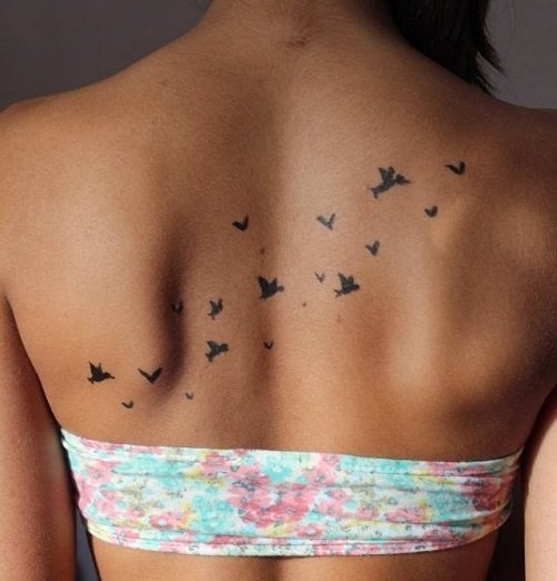 Una chica con su espalda tatuada con muchas aves pequeñas