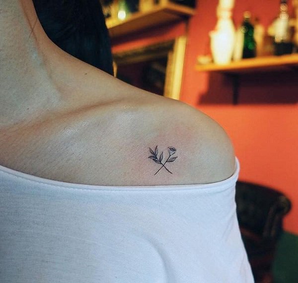 Tatuaje de una pequeña flor en el hombro de una joven mujer