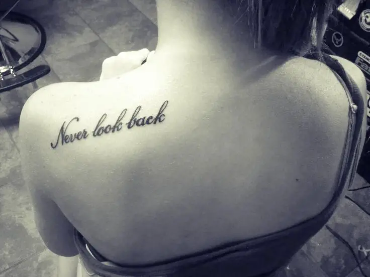 Frase tatuada en la espalda de una chica que dice: " Nunca mires atrás"