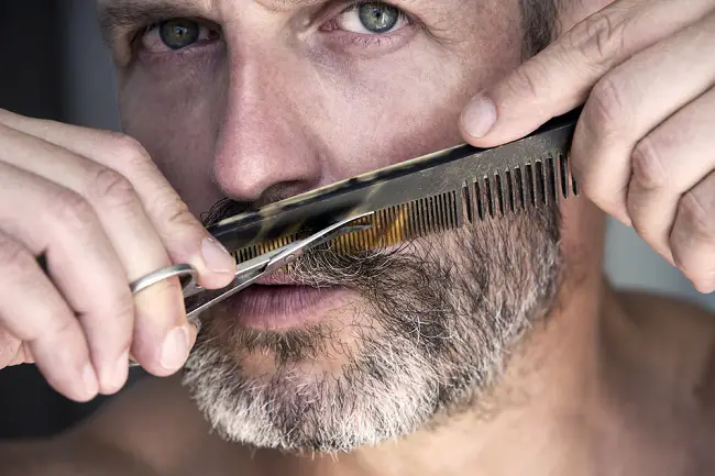 Hombre adulto peinando su barba que luce con canas