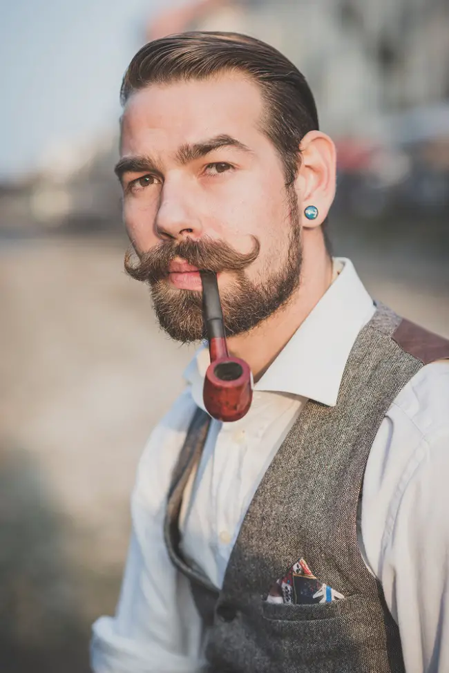 Joven con un look retro que ha dejado crecer su bigote y está fumando pipa