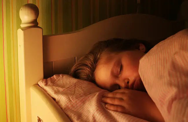 Mujer durmiendo sobre la cama con la luz del velador encendida