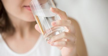 Mujer bebiendo agua tibia para beneficiarse de todas sus propiedades