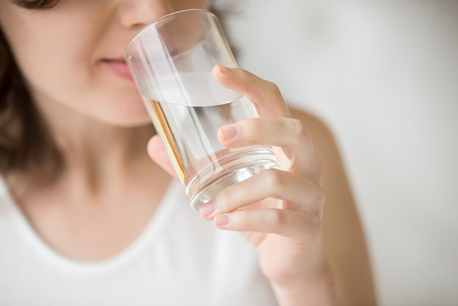 Mujer bebiendo agua tibia para beneficiarse de todas sus propiedades