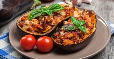 Unas berenjenas rellenas con arroz servidas en un plato acompañadas de tomate para una receta vegana imperdible