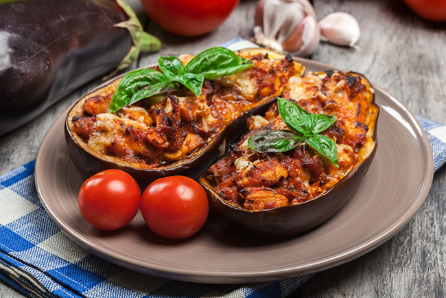 Unas berenjenas rellenas con arroz servidas en un plato acompañadas de tomate para una receta vegana imperdible