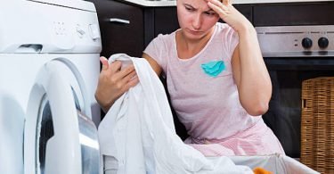 Mujer lavando la ropa en su lavadora para quitar las manchas y blanquearla