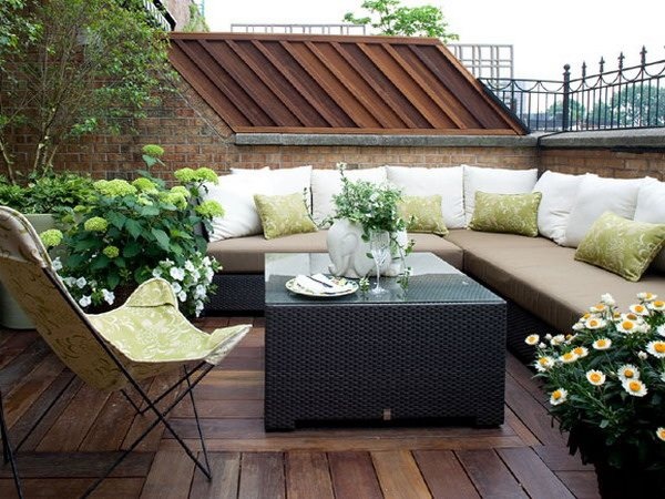 lindo detalle de terraza en la azotea decorado con muebles rústicos y cojines blancos con piso de madera y jardineras laterales.