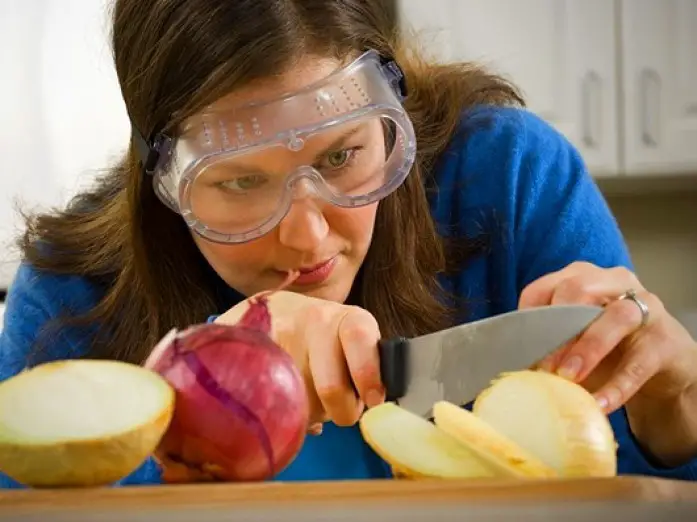 mujer con gafas para evitar llorar mientras corta las cebollas