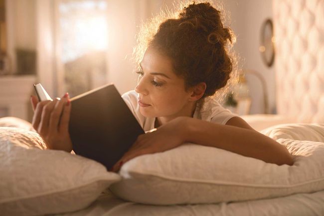 una mujer joven leyendo recostada sobre su cama