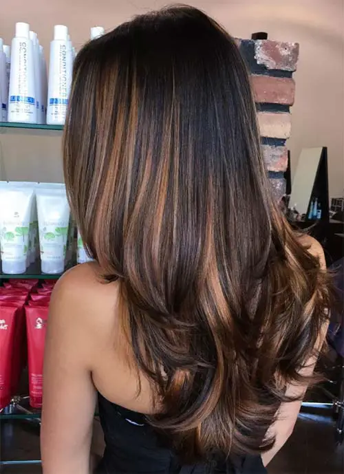 Chica con el cabello oscuro cortado en capas con mechas balayage en tonos cobre