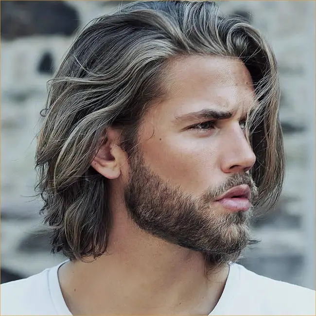 Hombre lleva un corte de cabello medio largo con toques platinados y barba