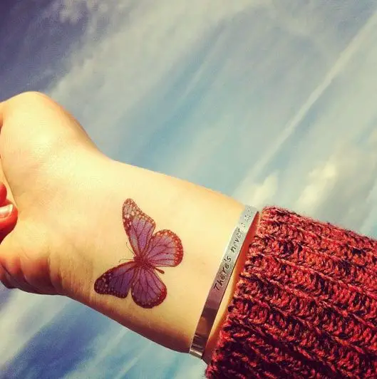un tatuaje de color rojo con el diseño de una mariposa en el brazo de una mujer