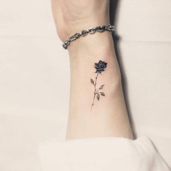 Mulher com braço tatuado segurando uma rosa pequena