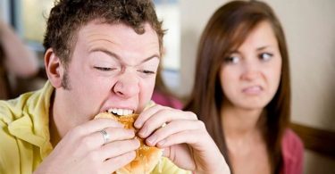 Hombre comiendo hamburguesa, mujer mal humor