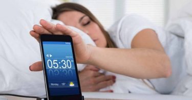 Mujer posponiendo alarma por no poder levantarse por las mañanas