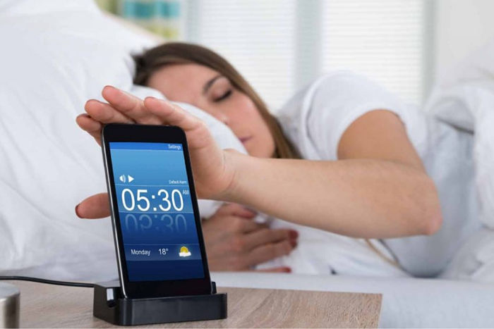 Mujer posponiendo alarma por no poder levantarse por las mañanas