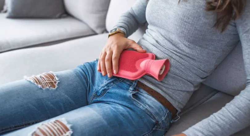 Mujer poniendo una bolsa de agua caliente en su vientre para aliviar el dolor menstrual