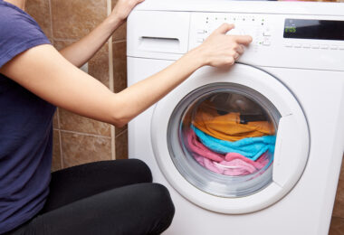 Mujer metiendo ropa para lavar en lavadora eléctrica