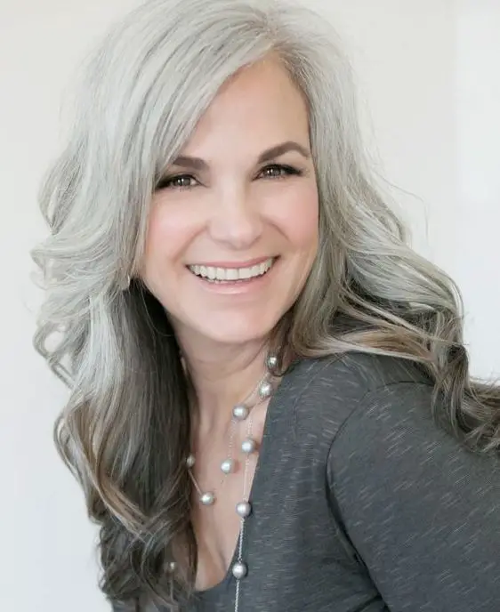 mujer sonriendo con canas usando una blusa gris cenizo