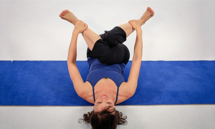 mujer haciendo postura de cara de vaca recostada yoga