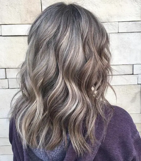 mujer de pelo largo y canoso con lowlights de espaldas blusa morada