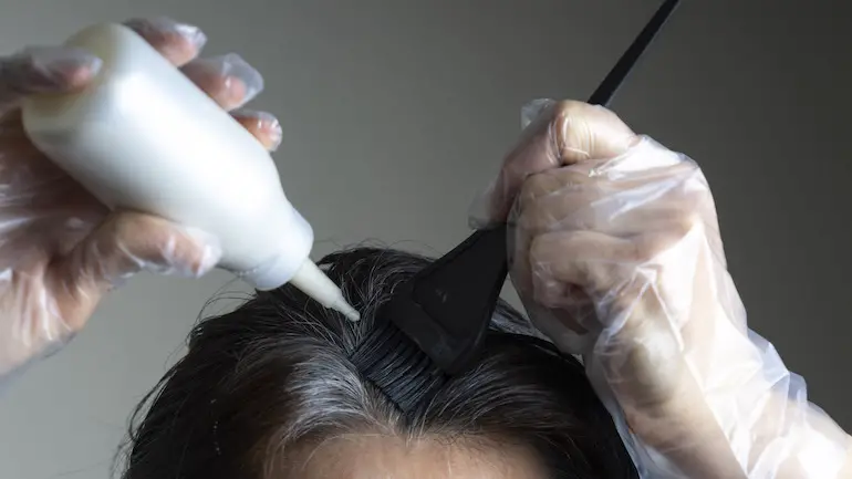 mujer de pelo negro con canas pintándose el pelo bote blanco de pintura de pelo brocha negra para pintar el pelo