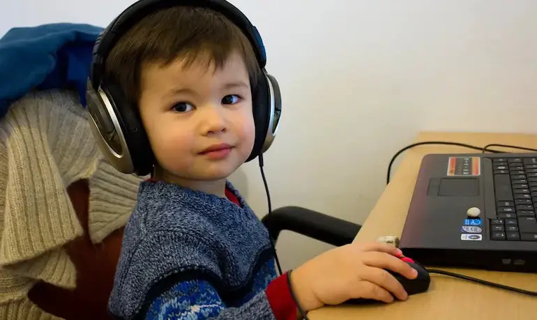 niño pequeño escuchando música con auriculares frente a laptop 