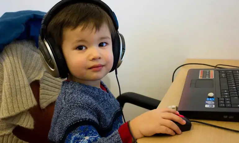 niño pequeño escuchando música con auriculares frente a laptop