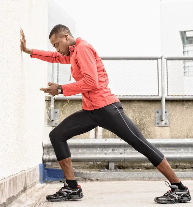 hombre afroamericano con ropa deportiva haciendo estiramientos de pantorrilla