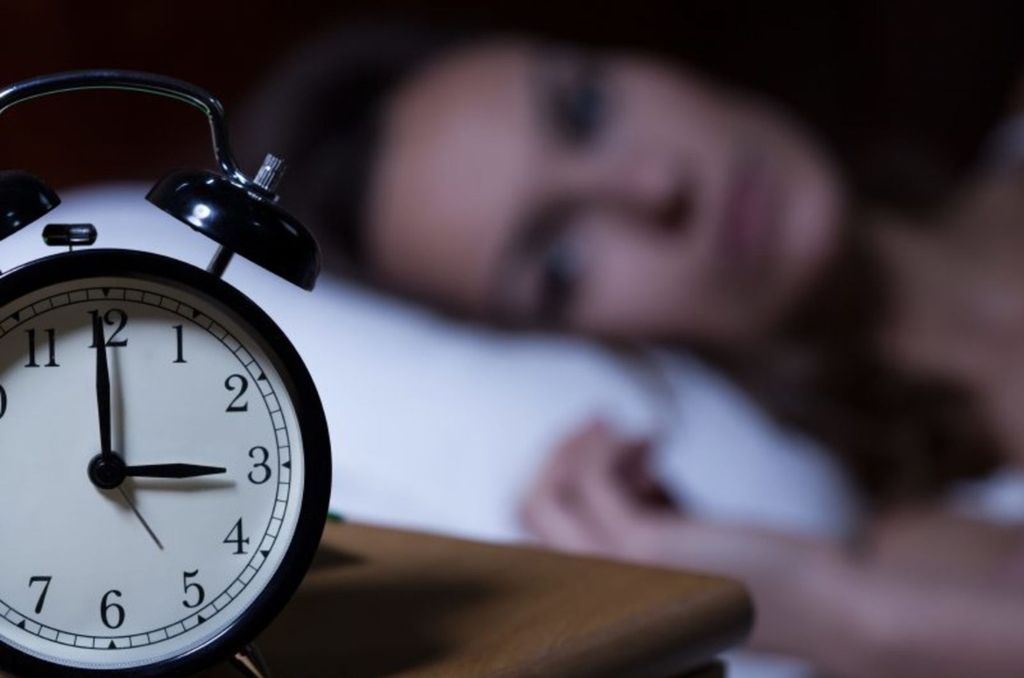 Mujer despierta mirando su reloj a las 3:00 de la mañana