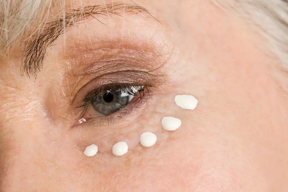 Mujer madura poniendo vitaminas en el cotorno de sus ojos